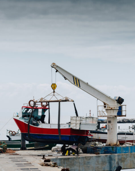 A red boat is in the water and a crane