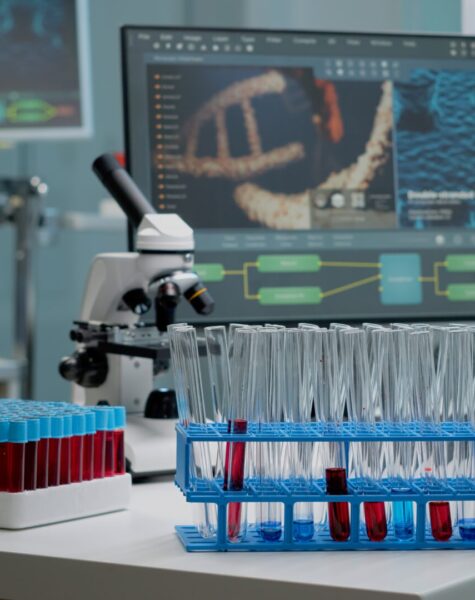 Medical test tubes with blood on desk in laboratory at research clinic. Biotechnology glassware, microscope and pipette as scientific equipment used for discovery in chemistry industry