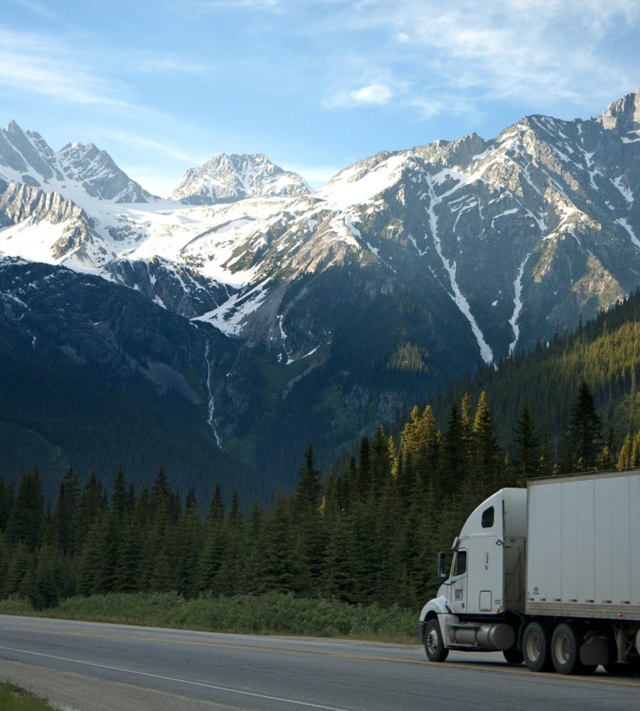 A white truck driving down the road near some mountains.